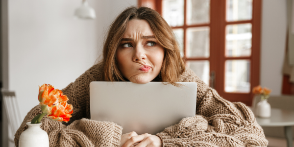 young woman with confused expression sat at laptop